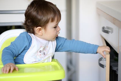 child in highchair opening a cupboard