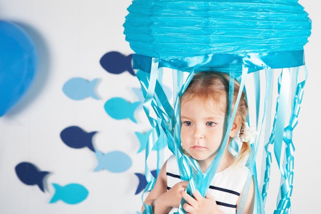 Girl standing under jellyfish party decoration made out of blue lampshade and ribbons for tentacles