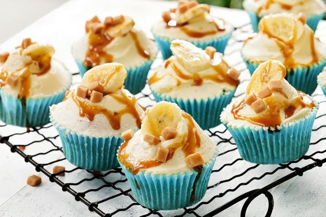 Cupcakes on a baking tray topped with icing, banana and toffee sauce