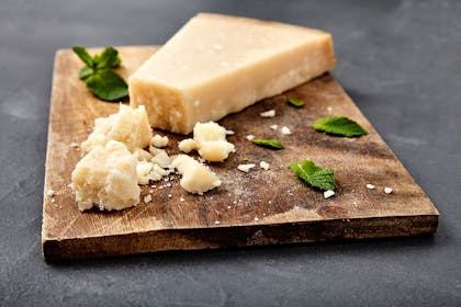 Slice of crumbling parmesan cheese on a wooden chopping board