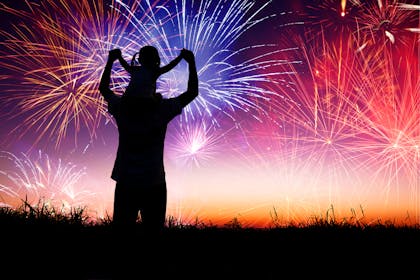 Silhouette of person watching fireworks with child on shoulder