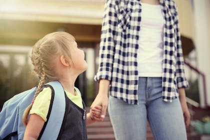 Girl in school uniform holding mum's hand