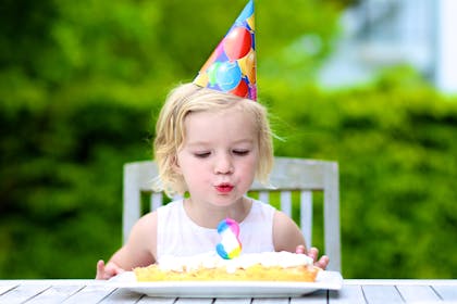 Girl wearing party hat blowing out candle on birthday cake