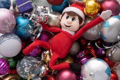 Elf on the Shelf lying in a pile of baubles and Christmas decorations