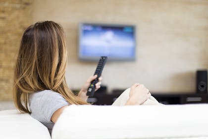 woman holding remote control watching TV - TV reviewer