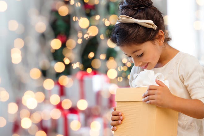 Little girl holding cardboard box in front of lit Christmas tree
