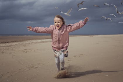 Girl in pink jacket running into the wind on a beach