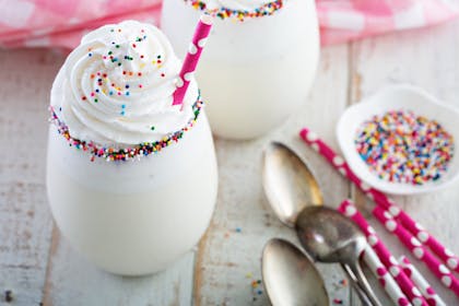 Vanilla milkshake with whipped cream, paper straws and party sprinkles