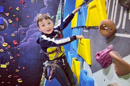 A young boy in a hoody pauses to smile at the camera while holding on to the wall at the The Boardroom Climbing  centre 