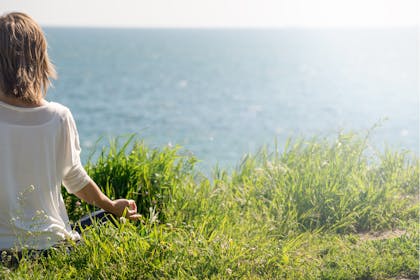 Woman meditating on grass by the sea