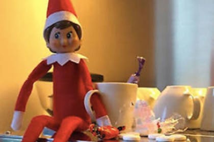 Elf sitting with his arm in links in the handle of a mug
