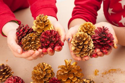 Kids holding red and gold painted pine cones