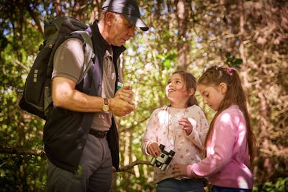 Two girls, one wearing a pair of binoculars around her neck, chat to a Forest Ranger in Thorpe Forest