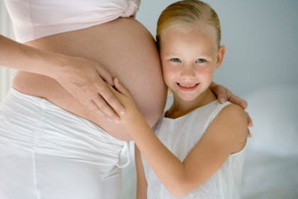 child in white hugging pregnant woman's belly