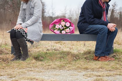 Couple on bench looking in opposite directions with bouquet of flowers between them