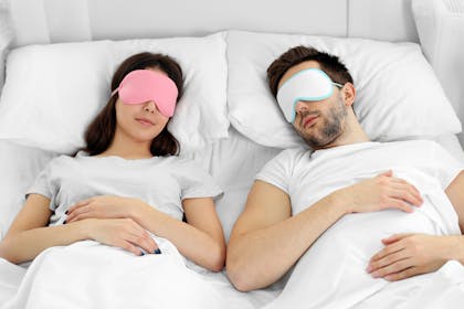 Couple asleep in bed wearing sleep masks