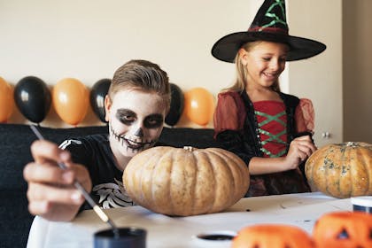 Children dressed in Halloween outfits decorating pumpkins