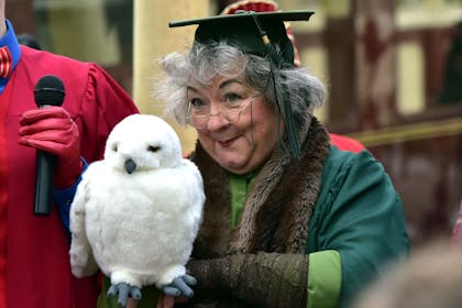 A kindly older teacher wearing a mortar board hat holds an owl, part of the Wizarding Adventure day at the East Lancashire Railway