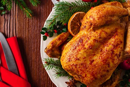 A roast chicken sits on a plate surrounded by festive accessories and a red napkin