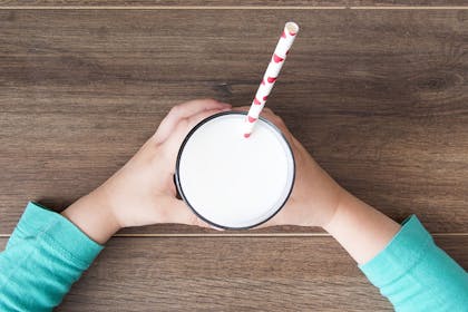 Child holding glass of milk with straw in it seen from above