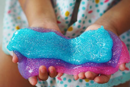Little girl's hands holding blue, purple and pink slime