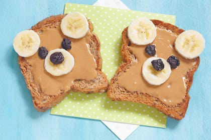 peanut butter on toast with banana slices for ears and raisins for eyes making it look like a bear