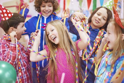 Children dancing at a party with streamers and hats