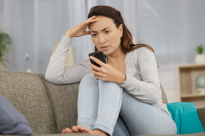 worried woman sitting on sofa looking at phone