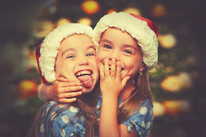 two girls wearing christmas hats hugging