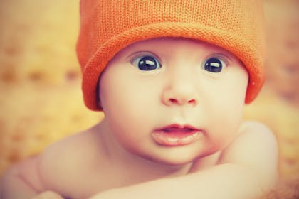 Baby with surprised expression wearing orange beanie hat