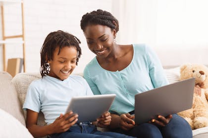 smiling mum and child sat on sofa holding a laptop and tablet