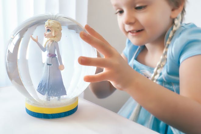 A little girl holds a snow globe with a toy Elsa figure inside