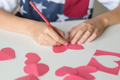 Kid drawing on red paper heart cutouts