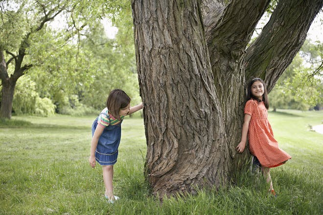 two girls playing hide and seek around a tree