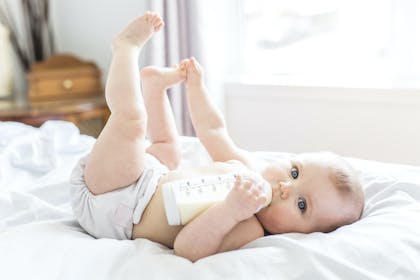 Baby drinking milk from bottle and touching toes 