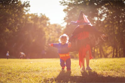 Two children dressed up in Halloween costumes running outside 