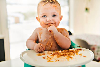 Baby eating spaghetti in highchair and making a mess