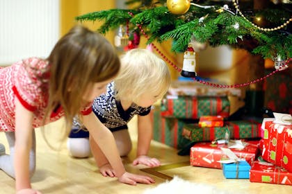 two children looking at presents under a Christmas tree