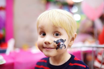 Toddler getting face painted with a skull and cross bones for Halloween