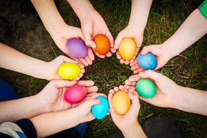 childrens hands all holding different coloured painted easter eggs