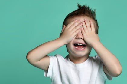 child with hands over his eyes on green background