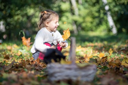A toddler plays in the autumn leaves near her witch's hat and basket