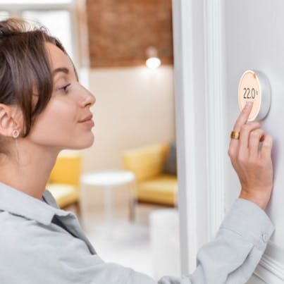 young smiling woman setting her thermostat to illustrate cost of energy bills