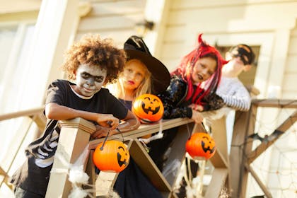 Kids dressed in costumes as a skeleton, a witch, a devil and a robber while carrying pumpkin buckets for a Halloween party