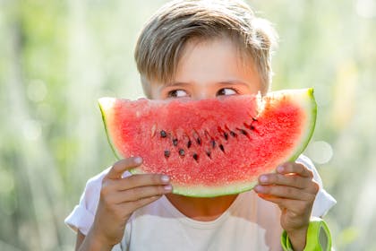 boy holding a slice of watermelon in front of his face