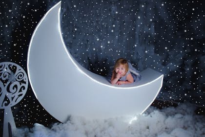 Little girl sits on glowing new moon
