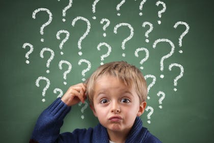 child standing next to blackboard with question marks written on it