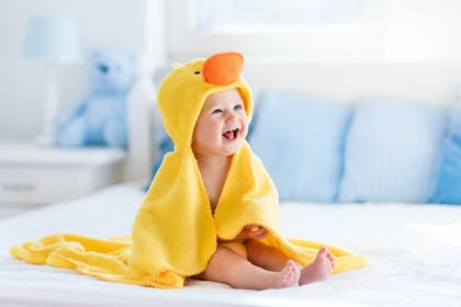 Baby girl laughing wearing yellow duck blanket after bath
