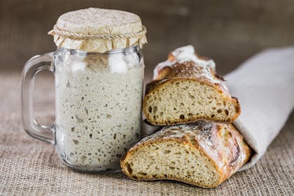 Sourdough starter in glass jar next to two loaves of sourdough bread