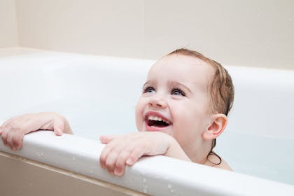 Toddler laughing and holding on to side of bath